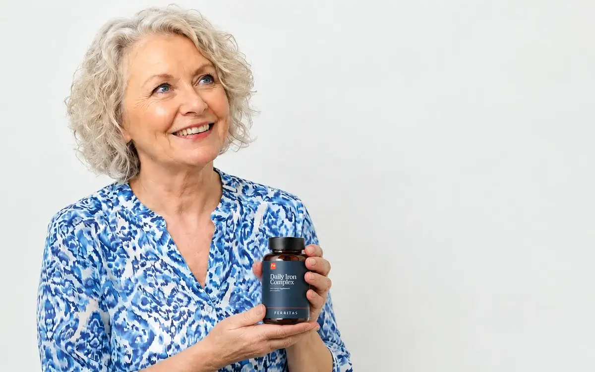 A smiling woman with curly grey hair holding a bottle of Ferritas Daily Iron Complex