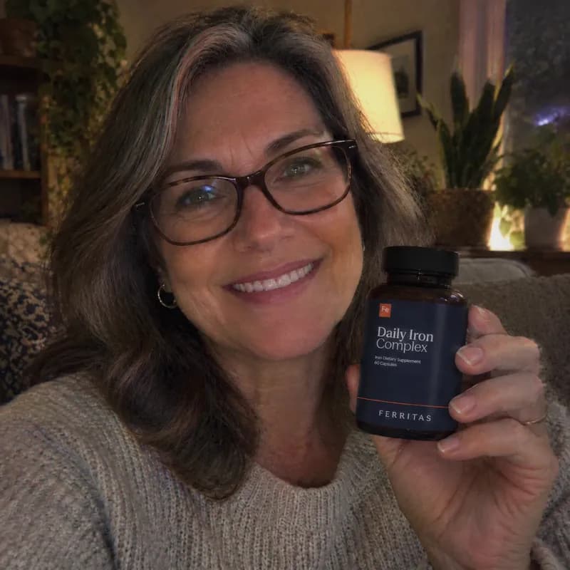 A smiling woman with glasses at home holding up a bottle of Ferritas