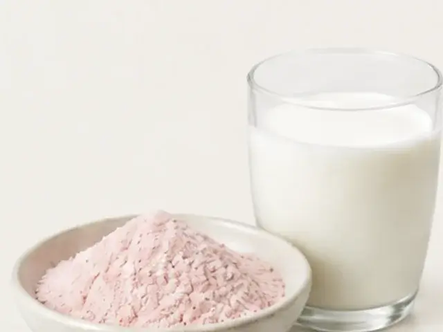 Pale lactoferrin powder in a bowl beside a glass of milk